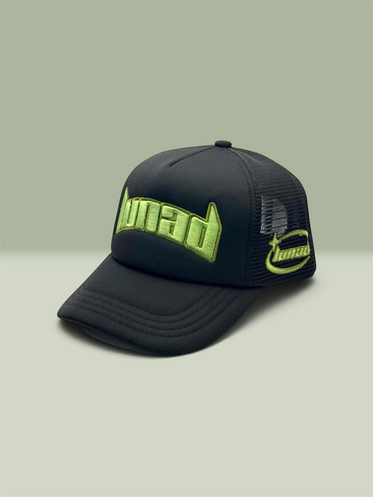 A black trucker-style baseball cap with sage green embroidered 'Lunad' lettering on the front and side, shown on a neutral light sage background.
