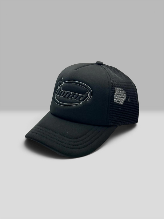 A black trucker-style cap with a curved brim, black mesh back panels, and a tonal black embroidered logo on the front, photographed on a light gray studio background.