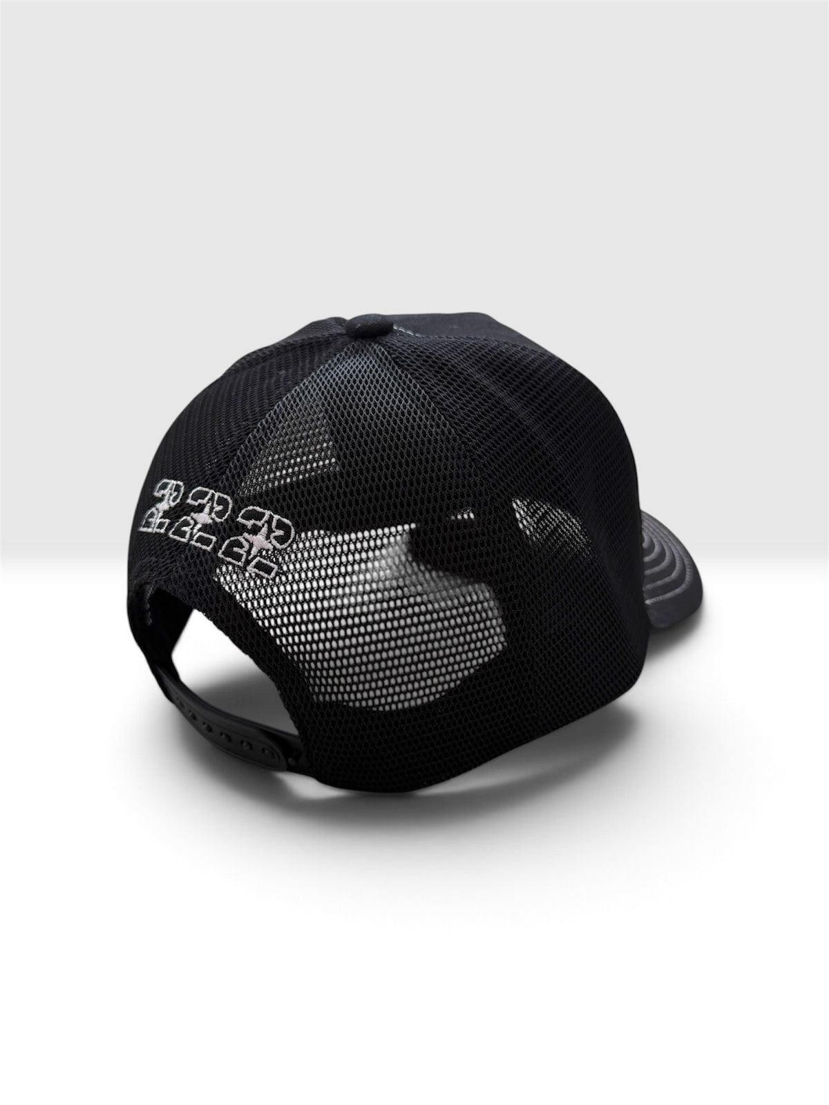 A black trucker-style baseball cap with a mesh back, shown from a rear three-quarter angle on a light gray background. The back panel features a white graphic logo that reads '222'.