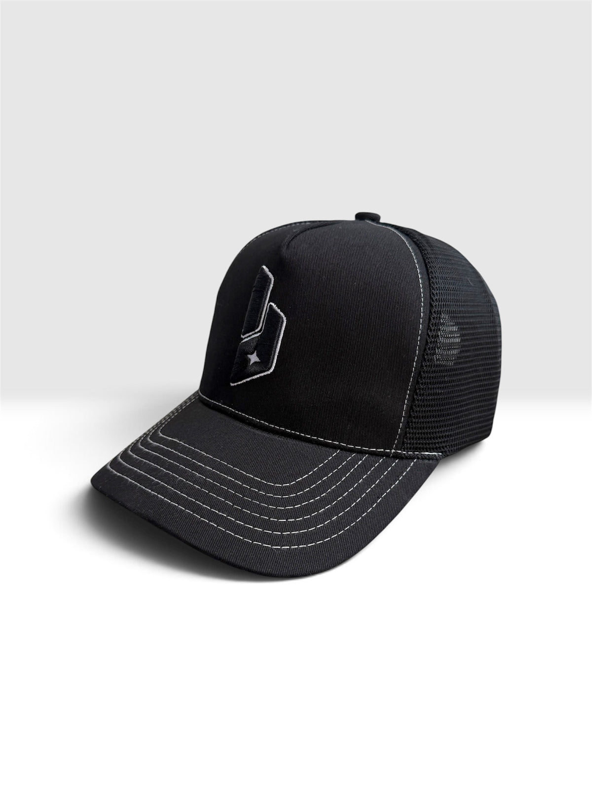A black trucker-style baseball cap with a curved brim, black mesh back, and white contrast stitching, featuring a stylized white logo on the front panel.
