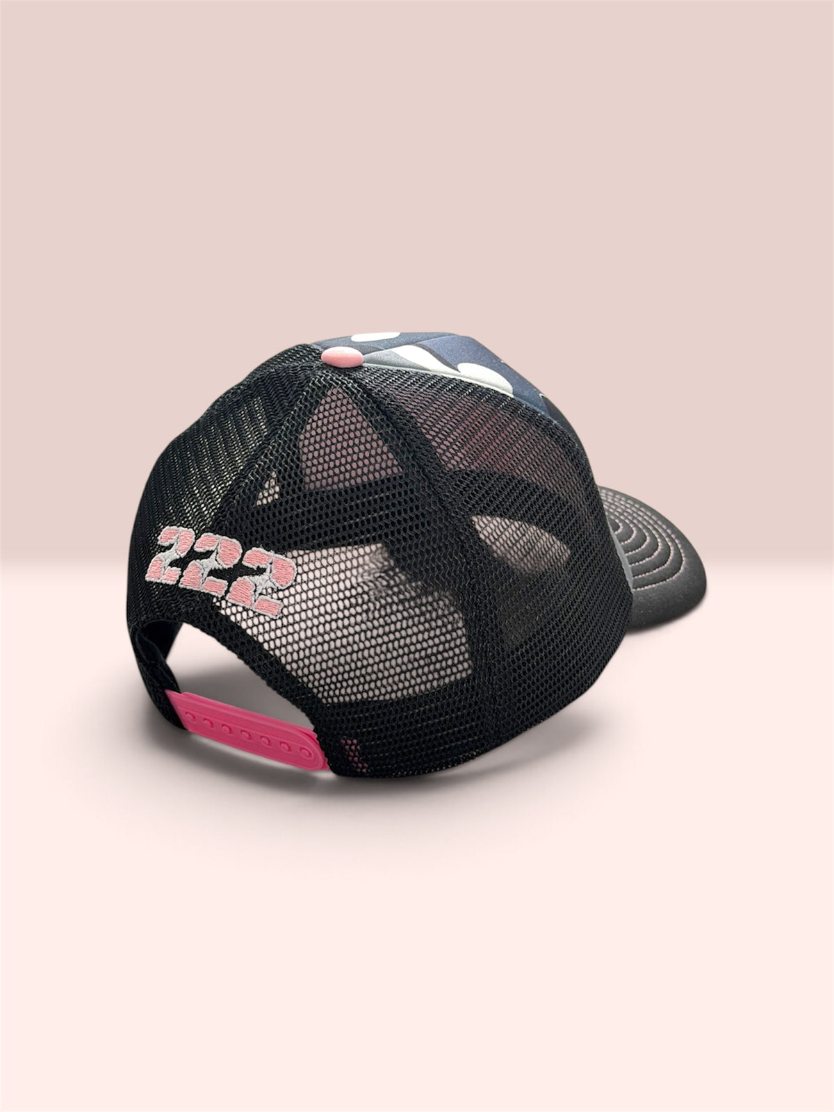A black mesh trucker cap shown from the back, featuring a curved brim, a pink '222' graphic on the rear, a pink back strap, and a small pink button on top.