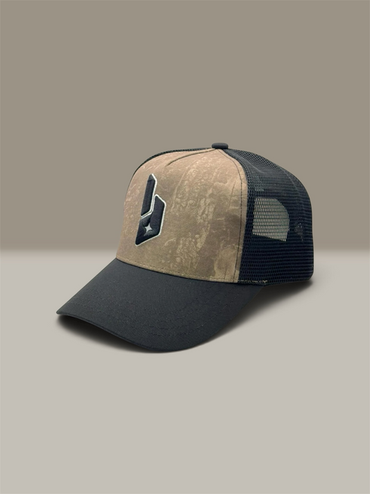A trucker-style baseball cap with a beige camouflage front panel, a dark black visor, and a dark black mesh back. The front panel features a dark black embroidered logo with a white star.